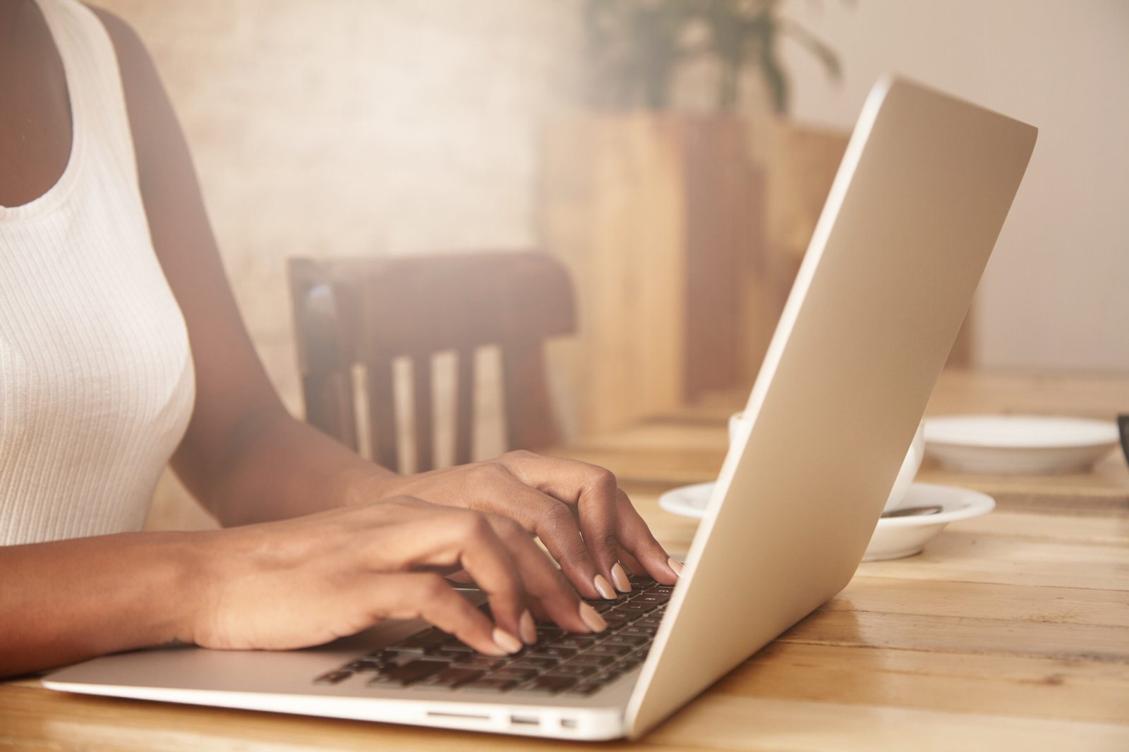Selective focus. Cropped shot of black woman's hands typing on keyboard while messaging friends via social networks using computer laptop. Female manager checking e-mail, sitting at the wooden table closeup female typing laptop keyboard scaled